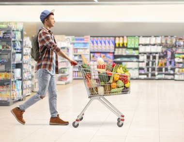 Bir erkek öğrencinin süpermarkette alışveriş arabasını iterken tam boy profil fotoğrafı.