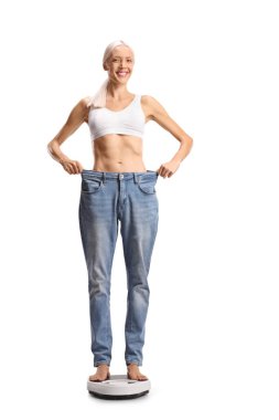 Beyaz arka planda izole bir ağırlık ölçeğinde duran büyük kotlu mutlu zayıf kadın.