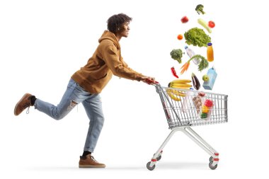 Full length profile shot of a young african american man running with a shopping cart and falling groceries isolated on white background clipart