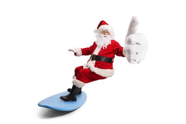 Noel Baba sörf tahtasına biniyor ve beyaz arka planda izole bir şekilde baş parmağını kaldırıyor.