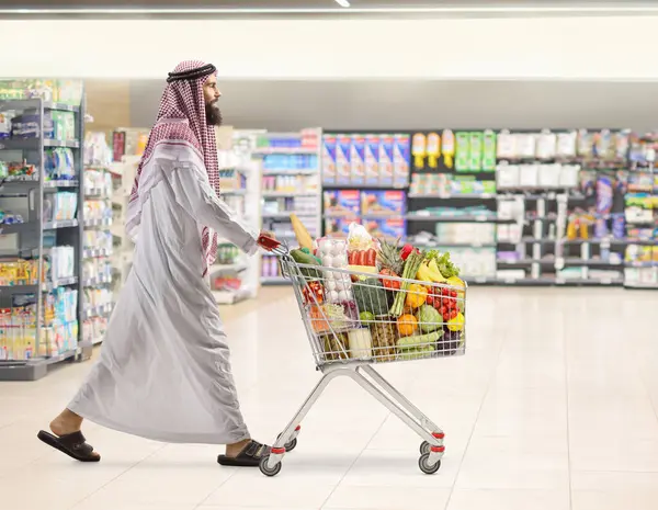 Suudi Arabistan 'lı bir adamın süpermarkette boş bir alışveriş arabasını iterken tam boy profil fotoğrafı.