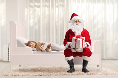 Yatakta uyuyan bir kız ve elinde hediye kutusuyla Noel Baba.