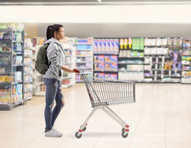 Markette boş alışveriş arabası olan bir kız öğrencinin tam boy profil fotoğrafı.