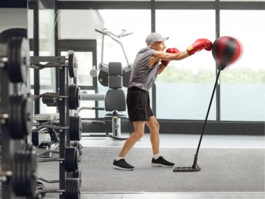 Yaşlı bir adam spor salonunda boks çantasını yumrukluyor.