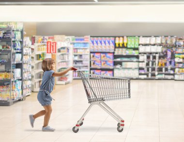 Küçük bir kızın süpermarkette alışveriş arabasını iterken tam boy profil fotoğrafı.