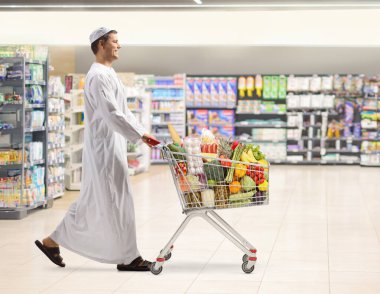 Bir süpermarkette yürüyen ve boş bir alışveriş arabasını iten Müslüman bir adam.