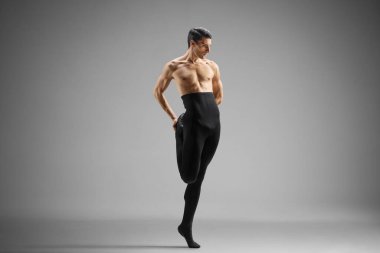 Siyah taytlı erkek balerin bacağını esnetiyor. Gri arka planda izole edilmiş.