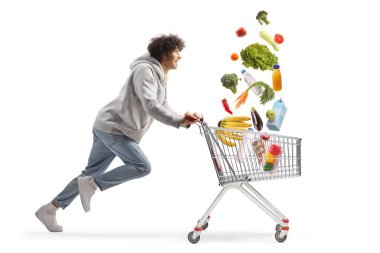 Markette koşan genç bir adam beyaz arka planda izole bir şekilde alışveriş arabasında düşüyor.