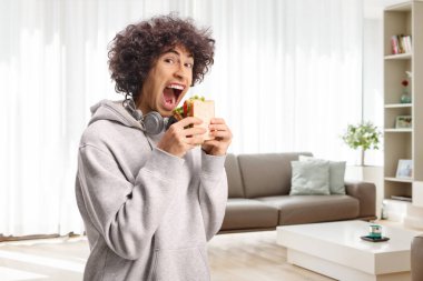 Ağzını açıp elinde sandviç tutan genç bir adam.