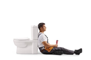 Beyaz arka planda izole edilmiş tuvaletin yanında oturan yorgun tesisatçı.