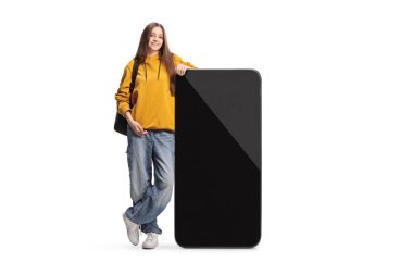 Beyaz arka planda izole edilmiş büyük bir akıllı telefona yaslanan genç kız öğrenci.