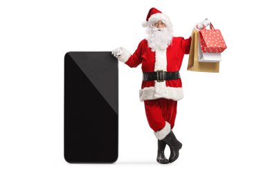 Santa claus leaning on a big mobile phone and holsing shopping bags isolated on white background clipart