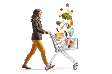 Genç bir kadının alışveriş arabasıyla yürüdüğü ve beyaz arka planda izole edilmiş alışveriş poşetlerinin düştüğü uzun bir profil çekimi.