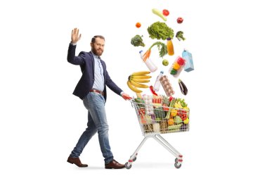 Alışveriş arabasıyla yürüyen, alışveriş yapan ve beyaz arka planda el sallayan bir adam.