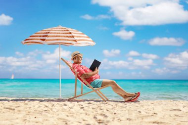 Turist kitap okuyor ve deniz kenarında bir sandalyede oturuyor.
