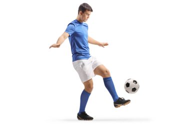 Mavi bluzlu ve beyaz şortlu futbolcu, beyaz arka planda izole edilmiş bir topu tekmeliyor.