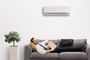 Klimanın altında bir kitapla kanepede uyuyan bir iş adamı.