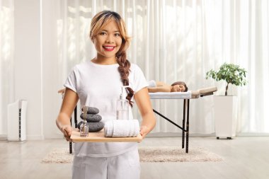 Masaj terapisti bir kaplıcada havlu, taş ve yağ tutuyor.