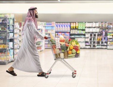 Arap bir adam süpermarkette alışveriş arabası itiyor.