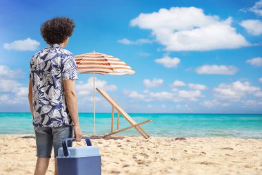 Portatif mini buzdolabı tutan ve sahilde denize bakan bir adam.