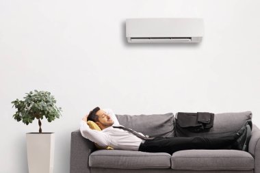 Klima ünitesinin altındaki kanepede dinlenen bir adam.