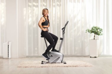 Genç Asyalı kadın evde spor bisikletinde oturuyor.