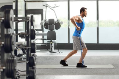 Direniş bandı olan bir adamın spor salonunda egzersiz yaparken tam boy profil fotoğrafı.