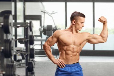Güçlü kaslı adam spor salonunda kaslarını esnetiyor.