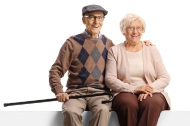 Boş bir panelde oturan ve beyaz arka planda izole edilmiş kameraya gülümseyen yaşlı çift.