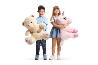 Beyaz arka planda izole edilmiş, elinde oyuncak ayı ve tek boynuzlu at tutan bir kızın tam boy portresi.