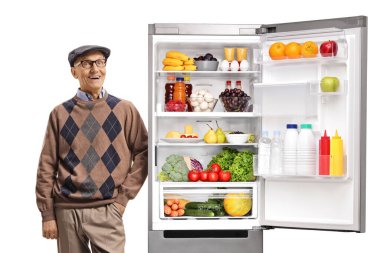 Beyaz arka planda izole edilmiş sağlıklı yiyeceklerle dolu açık bir buzdolabına yaslanan neşeli yaşlı adam.