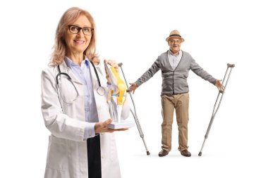 Diz kemiği mankeni olan bir doktor ve beyaz arka planda ameliyattan yeni çıkmış yaşlı bir erkek hasta.