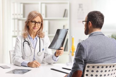 Kadın doktor ve erkek hasta ofiste röntgen görüntülerini kontrol ediyorlar.