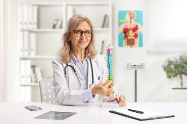 Ofiste omurga modeli olan bir kadın ortopedi doktoru var.