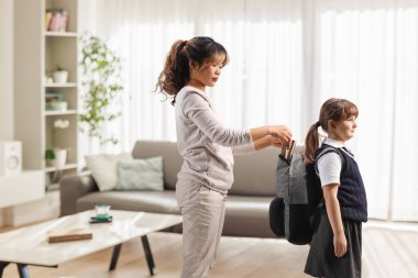 Dadı evde okul çantalı bir kıza yardım ediyor.