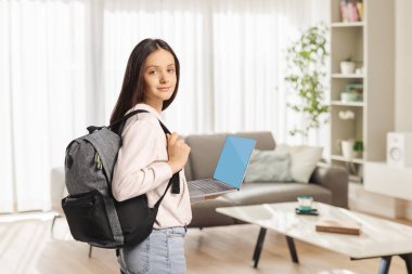 Sırt çantalı genç bir kız evde dizüstü bilgisayar tutuyor.