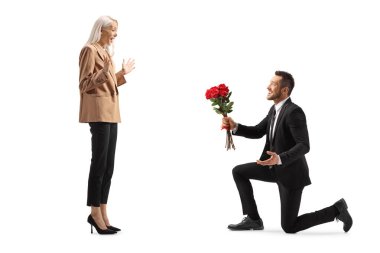 Adam beyaz arka planda soyutlanmış bir kadının önünde bir buket gülle diz çöküyor.
