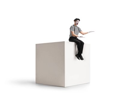 Pandomimci beyaz bir kübün üzerinde oturuyor ve elleri beyaz arkaplanda izole bir şekilde el kol hareketi yapıyor.