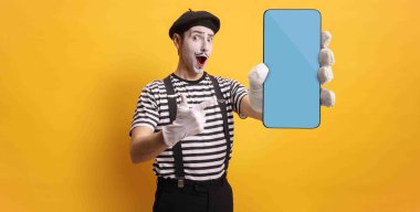 Sarı arka planda mavi ekranlı akıllı telefonu gösteren pandomimci