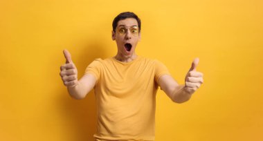 Mutlu ve neşeli genç adam sarı arka plana başparmak işareti yapıyor.