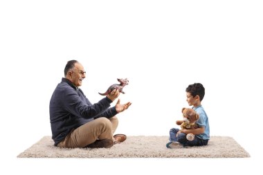 Olgun bir adam halının üzerinde oturuyor ve beyaz arka planda izole edilmiş bir çocukla oyuncaklarla oynuyor.