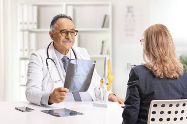 Ortopedik doktor ve bir kadın oturmuş diz kemiğinden gelen röntgen görüntülerini kontrol ediyorlar.