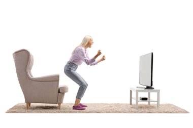 Beyaz arka planda izole edilmiş, elleri televizyonun önünde el kol hareketi yapan kendinden geçmiş bir kadının tam boy profil çekimi.