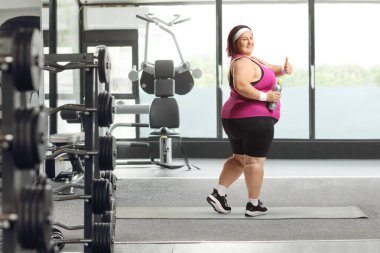 Spor giyim sektöründe şişman bir kadın elinde şişeyle baş parmağını kaldırıyor.
