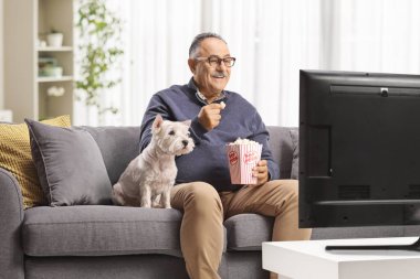 Yetişkin bir adam ve köpek televizyon seyrediyor ve patlamış mısır yiyor.