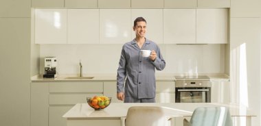 Mutfakta elinde bir fincan çayla pijamalı gülümseyen genç adam.