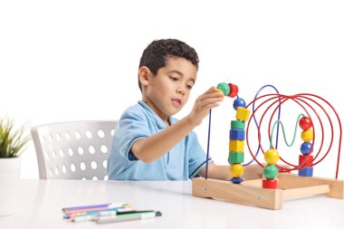 Masada oturan ve beyaz arka planda izole edilmiş oyuncak boncuk labirentiyle oynayan bir çocuk.