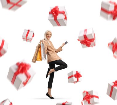 Alışveriş torbaları olan, gülümseyen ve kredi kartı kazanan bir kadın beyaz arka planda izole edilmiş hediyeler veriyor.