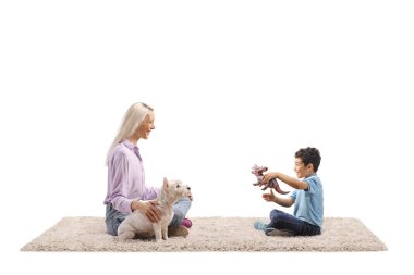 Batılı bir teriyerle halıda oturan ve beyaz arka planda izole edilmiş bir çocukla oynayan bir kadın.