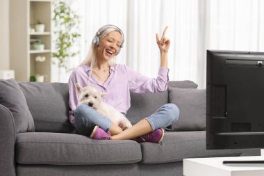 Kanepede oturan, bir köpeğe sarılan ve oturma odasında müzik dinleyen genç bir kadın.